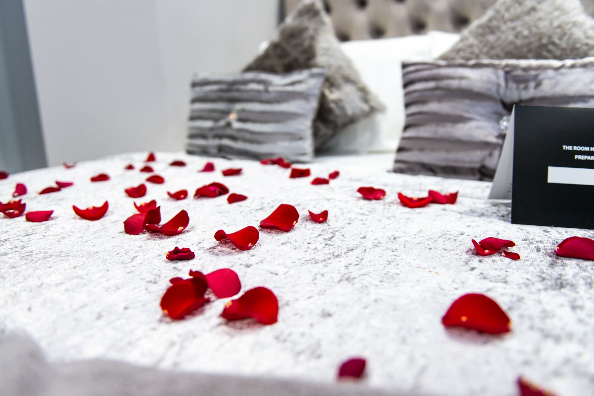 A bed with rose petals scattered on the surface, pillows, and a sign indicating room preparation.