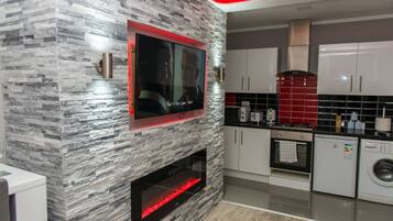 A modern kitchen with a built-in TV, a stone-textured wall, a fireplace, and a red-lit ceiling.