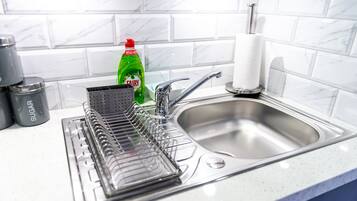 Una cocina con un escurreplatos, una botella de detergente Fairy y un recipiente para azúcar.