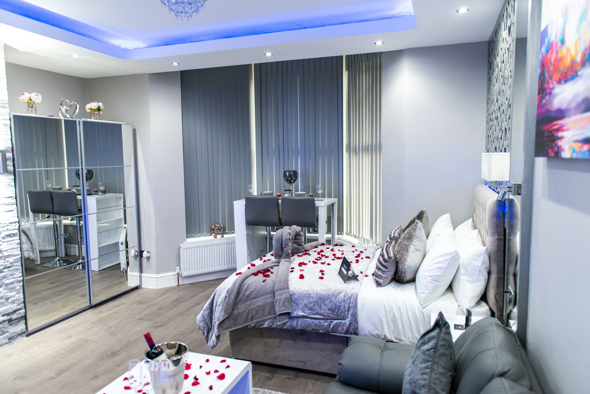 A modern bedroom with a large bed, a seating area, a vanity, and a mirrored closet.