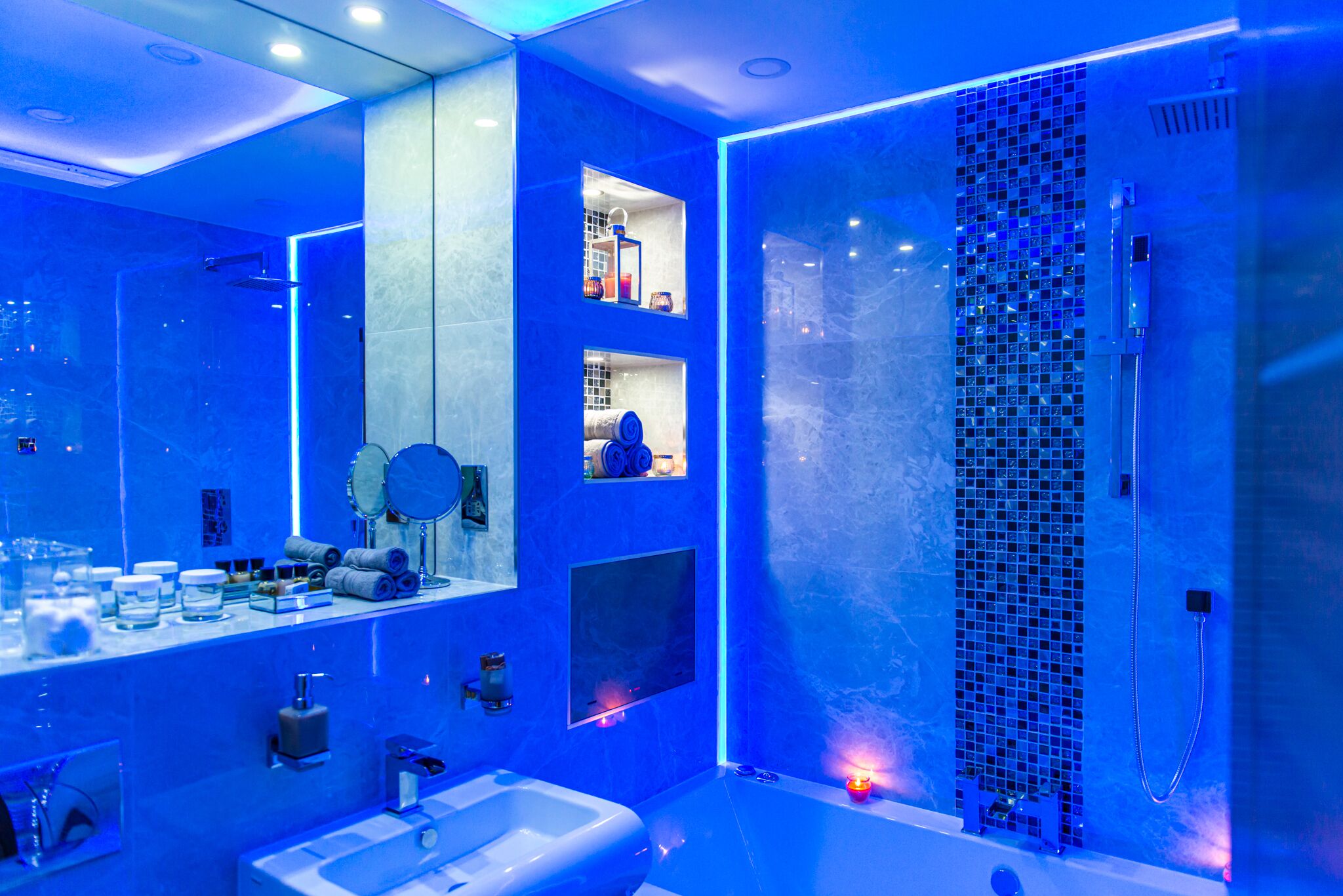 Un baño moderno con una decoración azul, un espejo grande, una bañera y una zona de ducha.