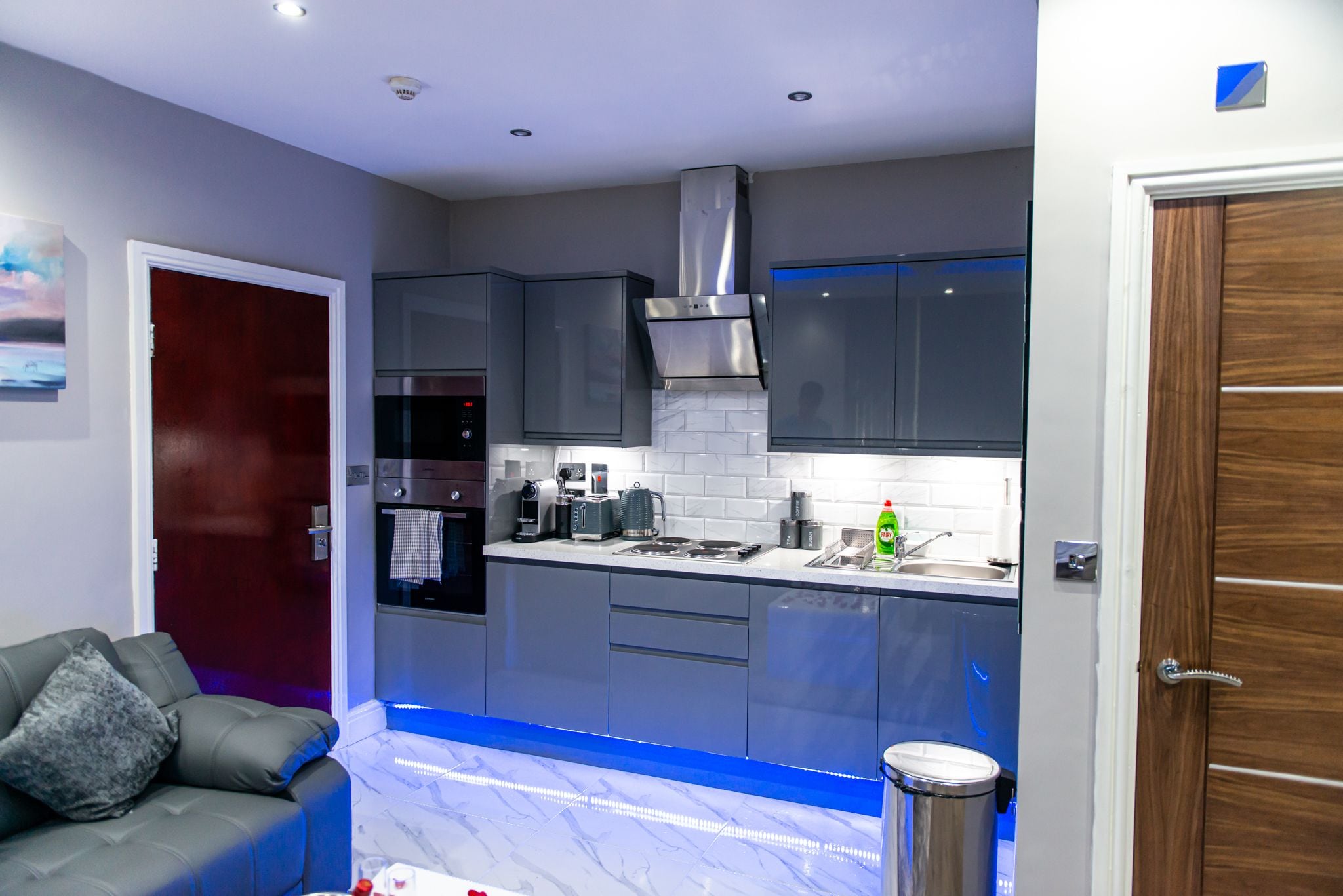 A modern kitchen with grey cabinets, a stainless steel range hood, and a marble countertop.