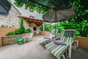 Un patio con dos sillones a rayas, una mesa, sillas, una sombrilla y un muro de piedra con plantas.
