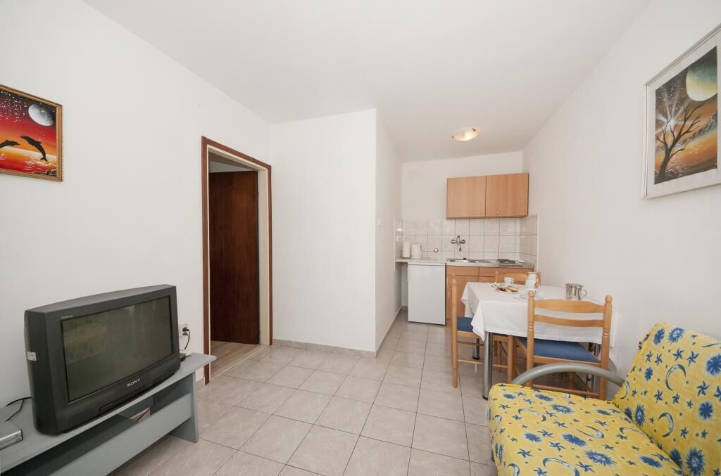 A compact living space with a television, a dining area, and a kitchenette.