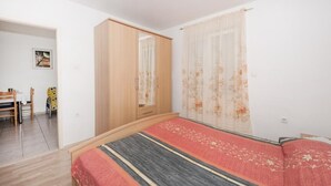 Un dormitorio con cama, armario, ventana con cortinas, una mesita con sillas y un cuadro en la pared.