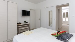 Ein Schlafzimmer mit einem Bett, einem an der Wand montierten Fernseher, einem Kleiderschrank und einer Tür zu einem anderen Raum.