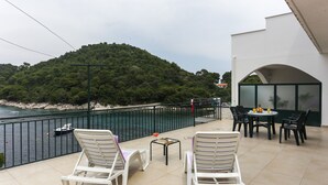 Een balkon met witte loungestoelen, een bijzettafeltje met boeken en uitzicht op een waterpartij en een beboste heuvel.