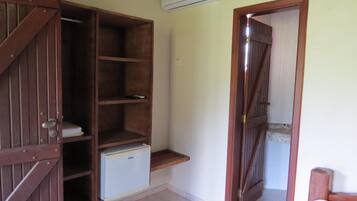 A room with a wooden wardrobe, a small white refrigerator, and a door leading to another room.
