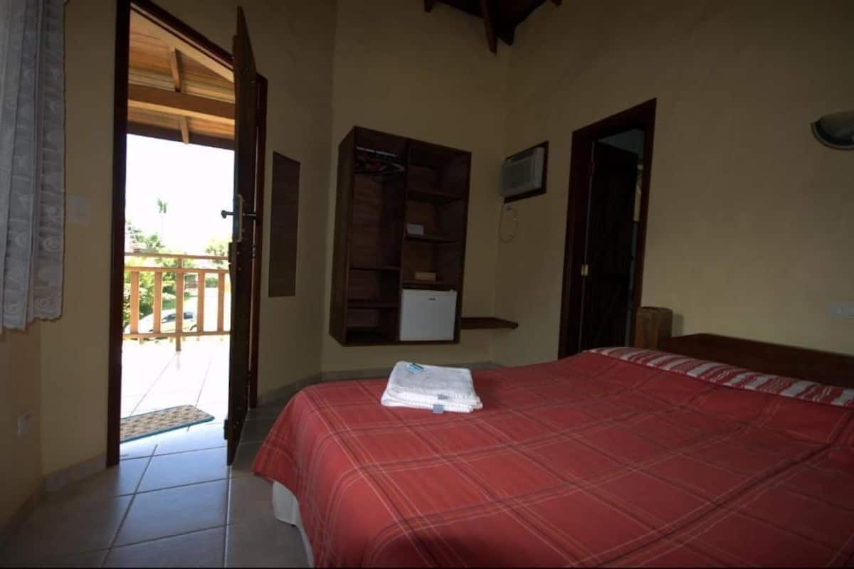 A bedroom with a bed, a wooden shelf, a door, and a small window.