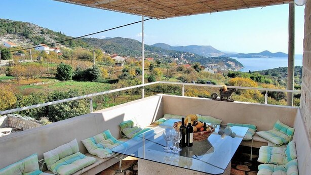 Eine Terrasse mit Glastisch, Sitzgelegenheit und Blick auf das Land und das Meer.