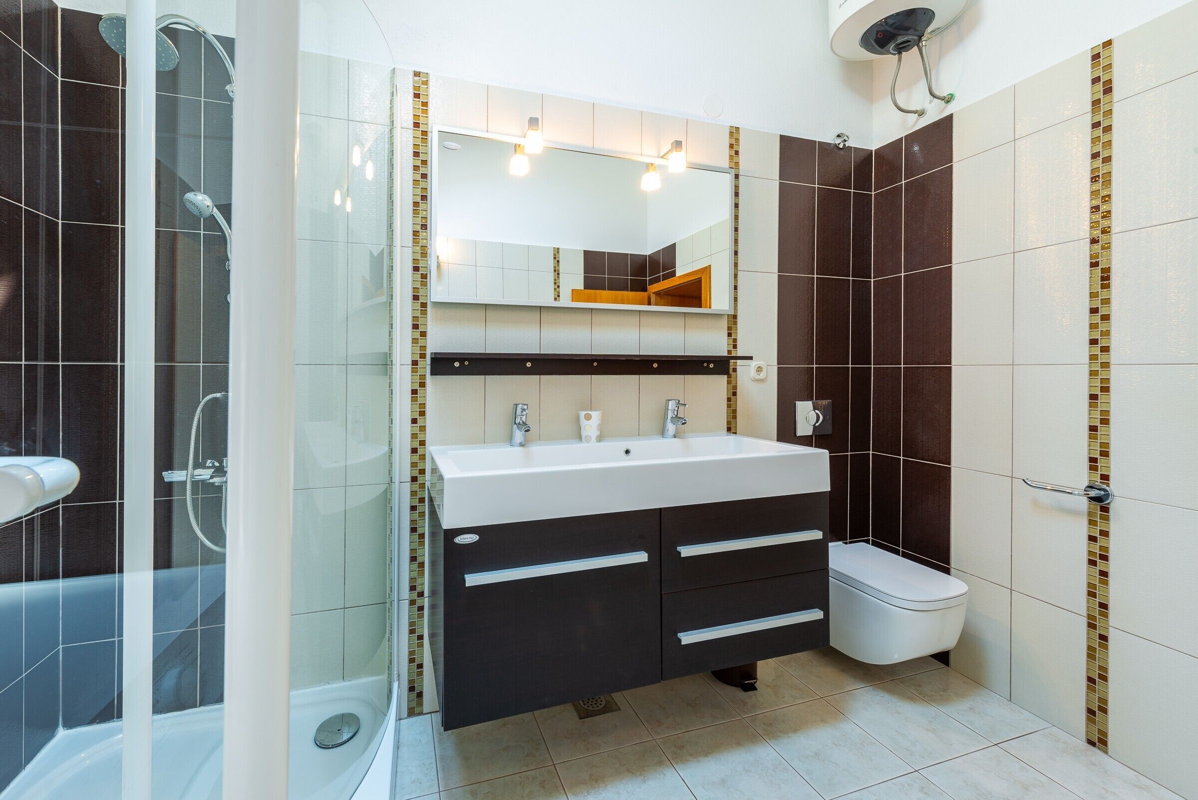 Et moderne badeværelse med en glasafskærmet brusekabine, en hvid vask med et spejl over, og et toilet.