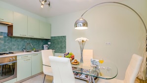 A modern kitchen with light green cabinets, a stainless steel stove, and a glass dining table with white chairs.