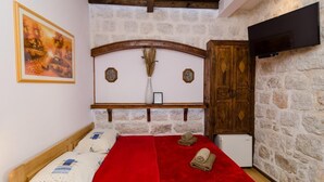 Una habitación acogedora con pared de piedra, cabecera de madera, televisor montado en la pared y cama con manta roja.