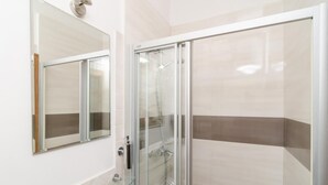 Un baño moderno con cabina de ducha de vidrio, tocador con tapa de cristal y un espejo grande.