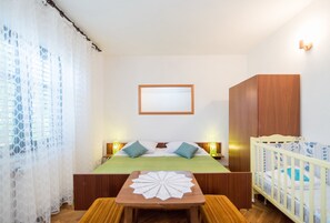 Une chambre à coucher comprenant un lit, des tables de chevet, un berceau, une armoire en bois et un cadre photo fixé au mur.