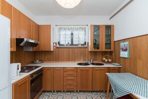 Une cuisine de taille modeste, dotée de meubles en bois, d’une cuisinière à gaz, d’un évier et d’une fenêtre ornée de rideaux en dentelle.
