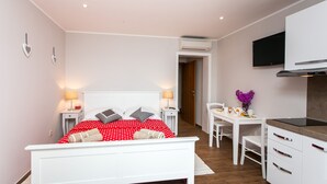 A modern bedroom with a white bed, red polka dot bedspread, and a white desk with a chair.