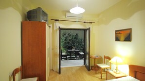 A hotel room with a bed, a desk with a lamp, a chair, a wardrobe, and a view of an outdoor area with a table and chairs. - Apartments Magda- Superior Studio Apartment with Patio and Garden View (Cavtat)