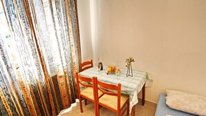 Un petit coin repas avec une table dressée pour deux personnes, une chaise, un vase rempli de fleurs et un panier de fruits.