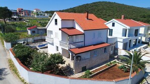 Un bâtiment à deux étages, doté d’un toit recouvert de tuiles rouges, d’un balcon et d’un jardin planté.