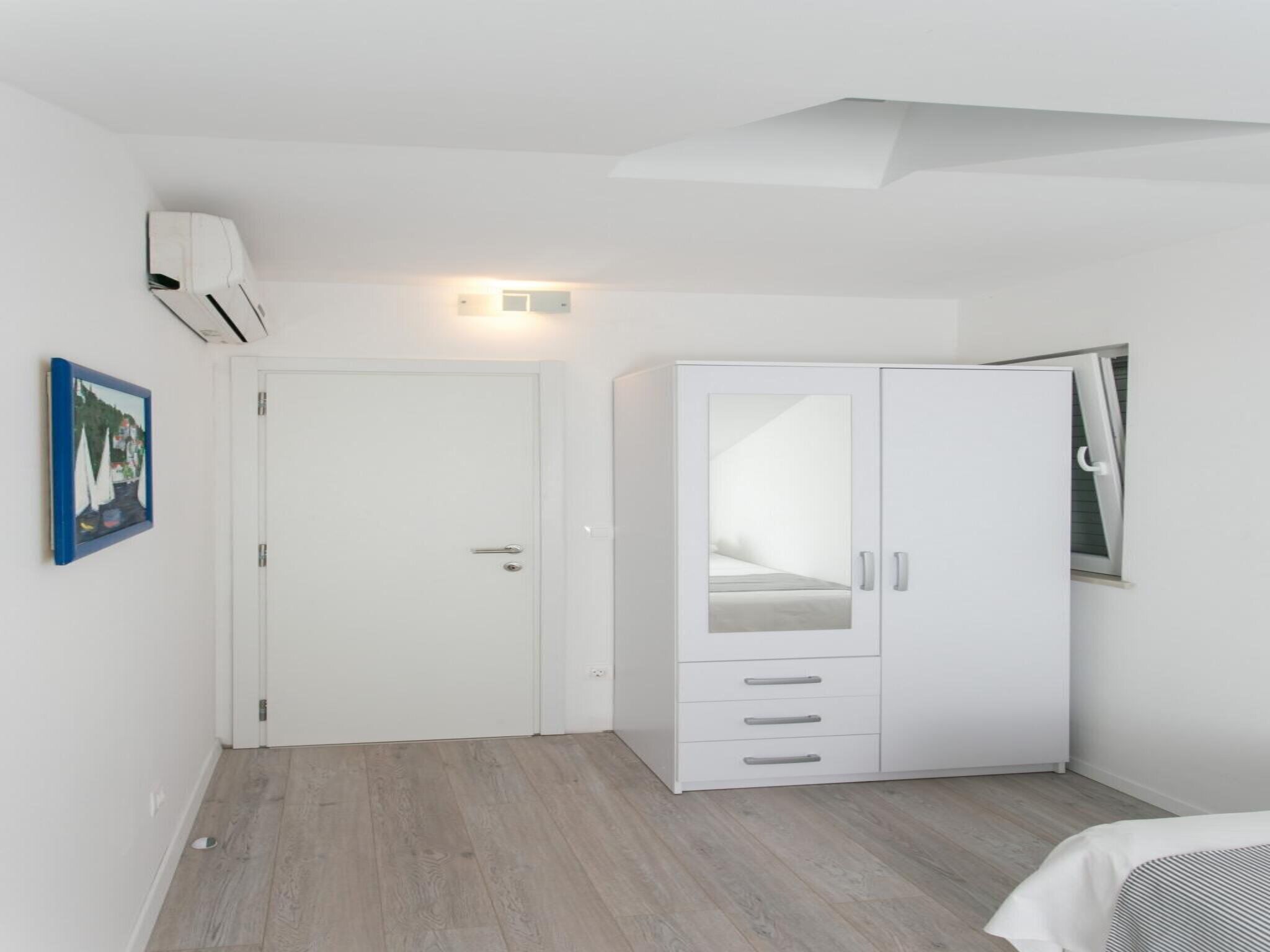 A minimalist bedroom with a white wardrobe, a door, and a framed picture on the wall.