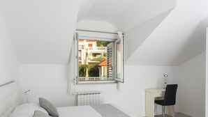 Un dormitorio con cama, escritorio, silla y ventana que ofrece vistas abiertas de edificios.