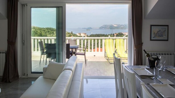 Una sala de estar moderna con un sofá, una mesa de comedor lista para dos personas y un balcón con vista al mar.