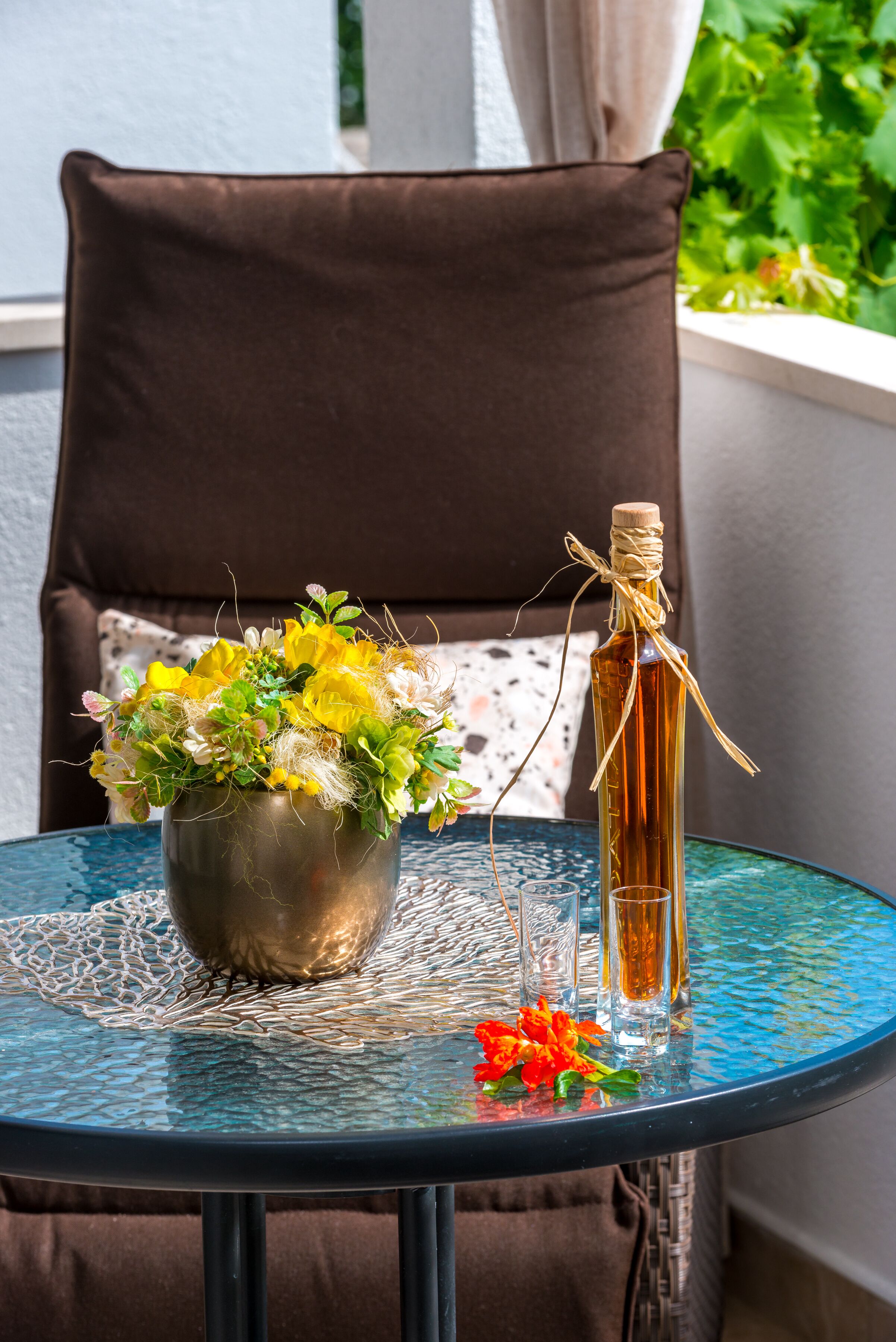 A round glass table with a metal vase of yellow and white flowers, a clear glass bottle with a cork, and a small red flower on the table. - Guest House Kuna - Comfort double room (Dubrovnik)