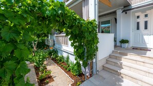 A residential garden with a grapevine arching over a pathway leading to a white house with a balcony. - Guest House Kuna - Comfort double room (Dubrovnik)