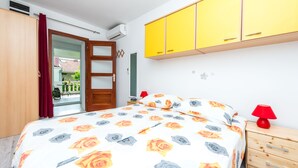 A bedroom with a bed, a wooden wardrobe, a yellow cabinet, a red lamp, and a view of the outside. - Guest House Kuna - Comfort double room (Dubrovnik)