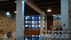 A bar area with shelves of bottles, a round table with glasses, and a stone wall.