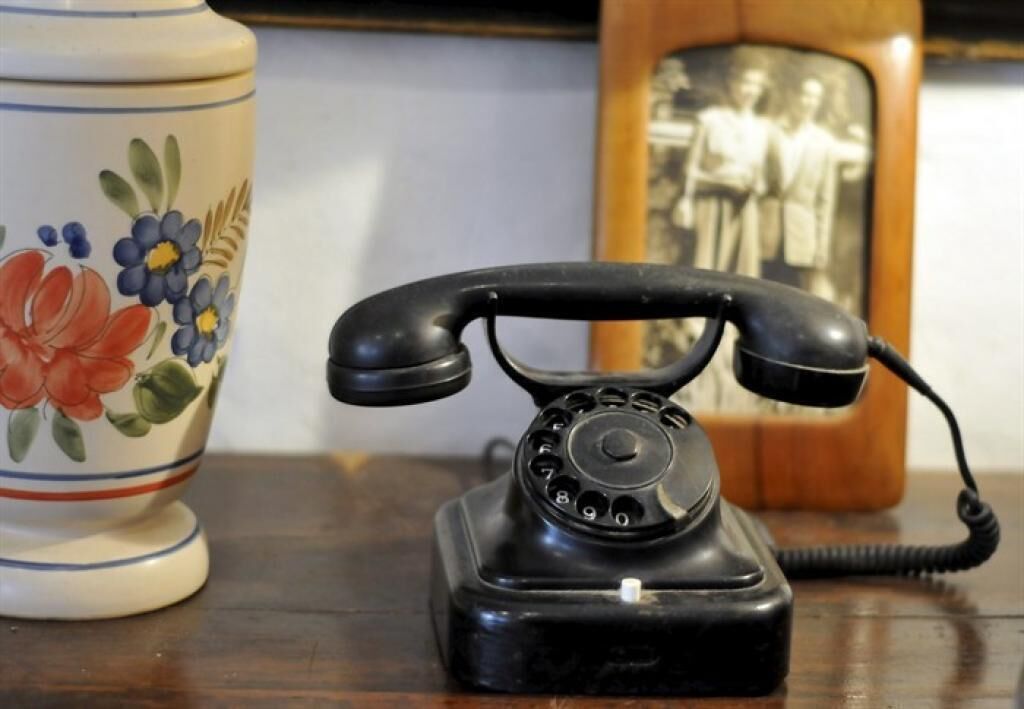Um telefone antigo com discador rotativo preto sobre uma superfície de madeira.