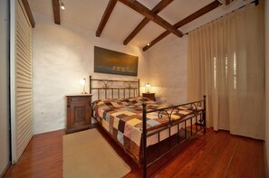 A bedroom with a wooden bed, a nightstand, a painting on the wall, and a window with curtains.