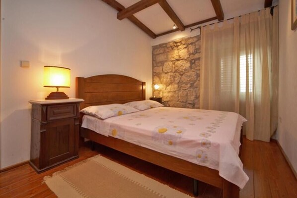 Une chambre avec un lit en bois, une table de chevet avec une lampe, un mur en pierre et une fenêtre avec des rideaux.