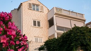 Ein mehrstöckiges Gebäude mit beige-farbener Fassade, weißen Fensterläden und einem Balkon mit Geländer.