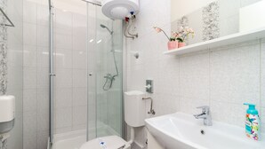 Une salle de bain moderne avec une douche à parois de verre, des toilettes blanches, un lavabo avec un robinet et un porte-rouleau de papier toilette.