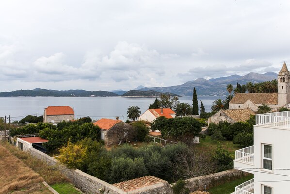 A coastal village with traditional stone buildings, a church, and a view of the sea and mountains.