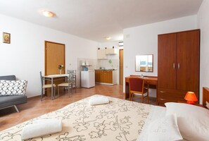 A compact hotel room with a bed, a desk, a kitchenette, and a sofa.