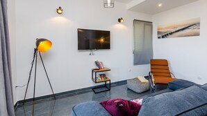 A modern living room with a flat-screen TV, a standing lamp, a sofa, a chair, and a bookshelf. - Villa Bell Memories- Two Bedroom Apartment with Balcony and Sea View (Cavtat)