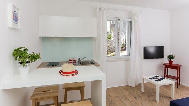 Una cocina compacta con encimera blanca, un lavamanos y una ventana con cortinas.