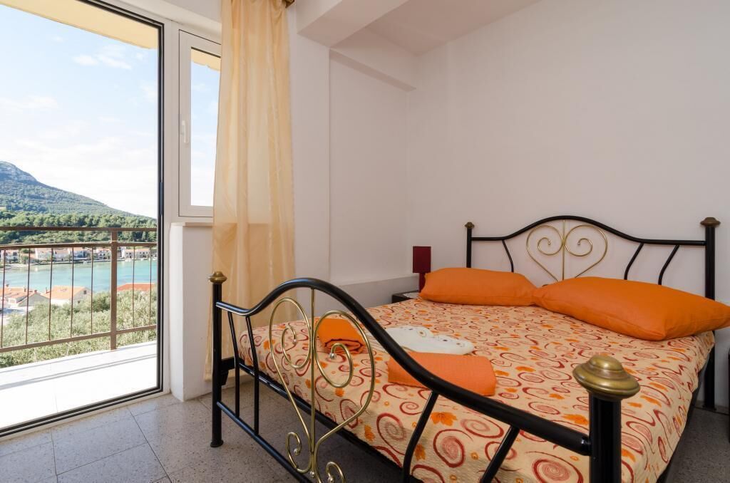 Een slaapkamer met een bed, een raam met uitzicht op een meer en bergen, en een balkon.