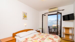 A bedroom with a bed, a bedside table, a TV mounted on the wall, and a balcony with a view.