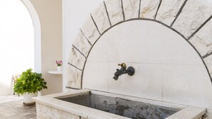 A stone-tiled outdoor sink with a faucet, surrounded by a stone arch.