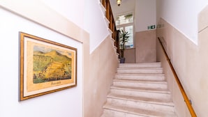 Un escalier avec une rampe en bois, un tableau encadré au mur et une plante en pot tout en haut.
