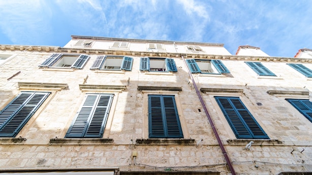 Un immeuble à plusieurs étages, doté d’une façade en pierre et de nombreuses fenêtres équipées de volets.