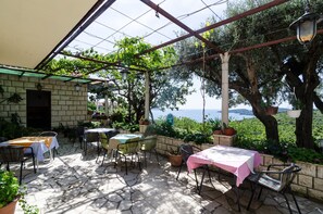 Eine Terrasse im Freien mit Steinboden, Tischen mit Tischdecken und Stühlen.