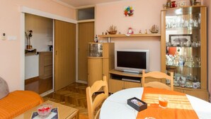 Un ambiente compatto con TV, tavolo da pranzo e una vetrina contenente oggetti decorativi.