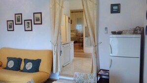 A living room with a sofa and a small table, a kitchen with a refrigerator, and a bedroom visible through a doorway. - Apartment Agata - Two Bedroom Apartment with Terrace and Sea View (ST) (Splitska)