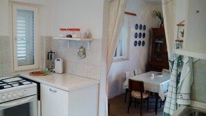 A compact kitchen with a gas stove, a small refrigerator, and a dining area with a table and chairs. - Apartment Agata - Two Bedroom Apartment with Terrace and Sea View (ST) (Splitska)