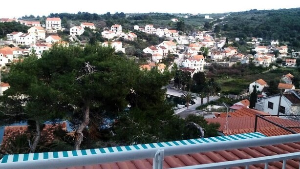 A coastal town with terracotta-roofed buildings, a prominent pine tree in the foreground, and a balcony railing. - Apartment Agata - Two Bedroom Apartment with Terrace and Sea View (ST) (Splitska)